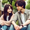 A Japanese couple enjoying a casual and relaxed moment, inspired by the style of Ueto Aya and HIRO's love story. They are outside, perhaps in a beautiful garden or quiet city park, reflecting the beginning of their relationship. The scene is soft, with natural colors, and highlights the warmth and subtle connection between them. 16:9 aspect ratio.