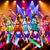 A 6-member Japanese idol group with unique member colors, performing energetically on stage with vibrant lighting. The members are wearing colorful outfits corresponding to their member colors, singing and dancing with enthusiasm. The audience is waving glow sticks matching the members' colors. The atmosphere is lively and exciting.